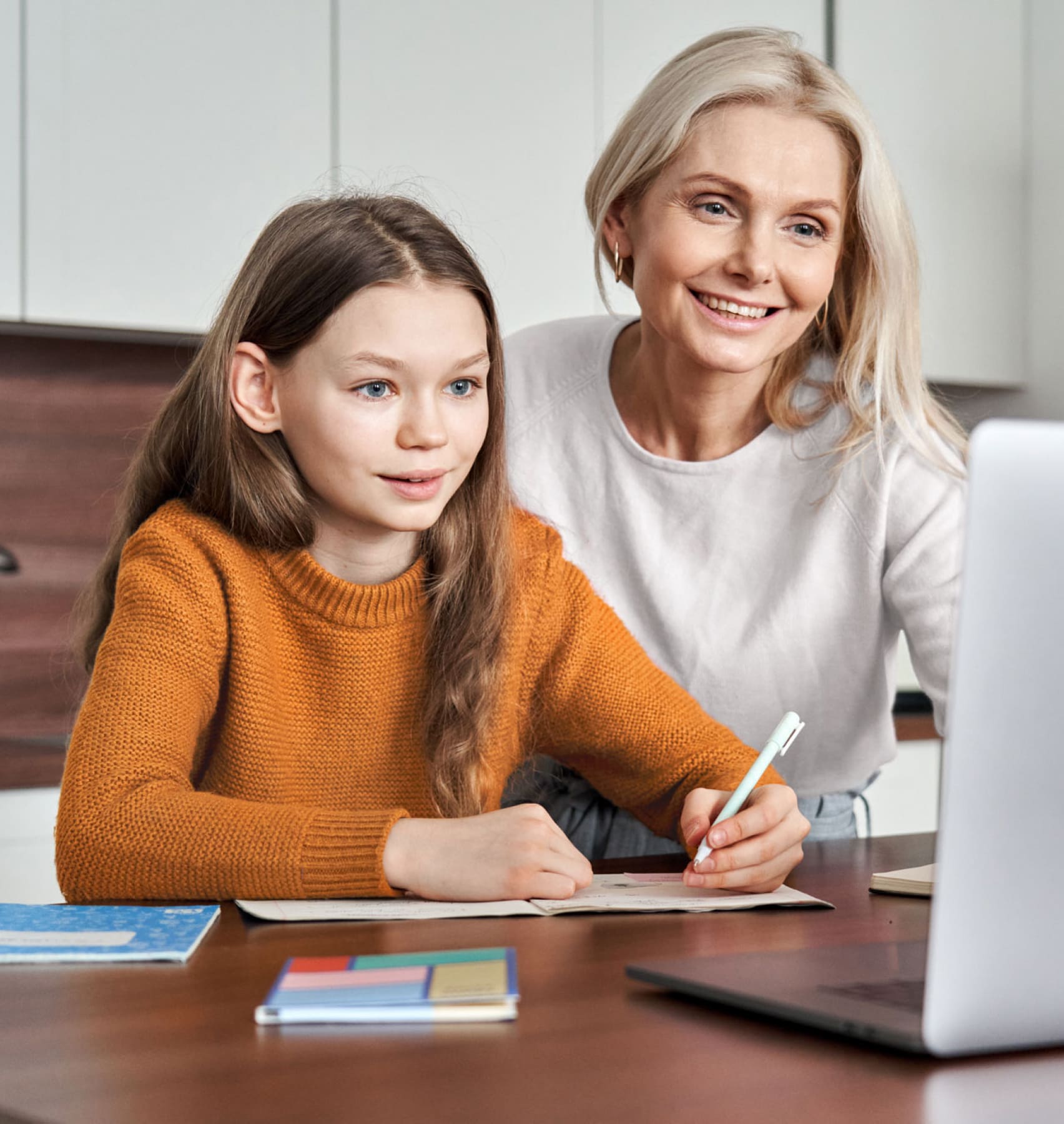 A woman and a young girl are seated at a table, engaged with a laptop in front of them.