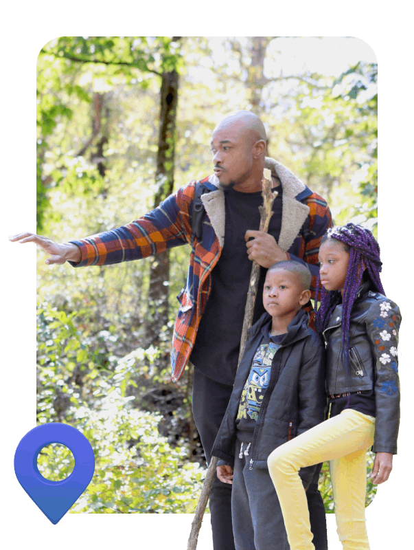 A man stands in the woods with two children, surrounded by trees and natural greenery, enjoying a moment together.